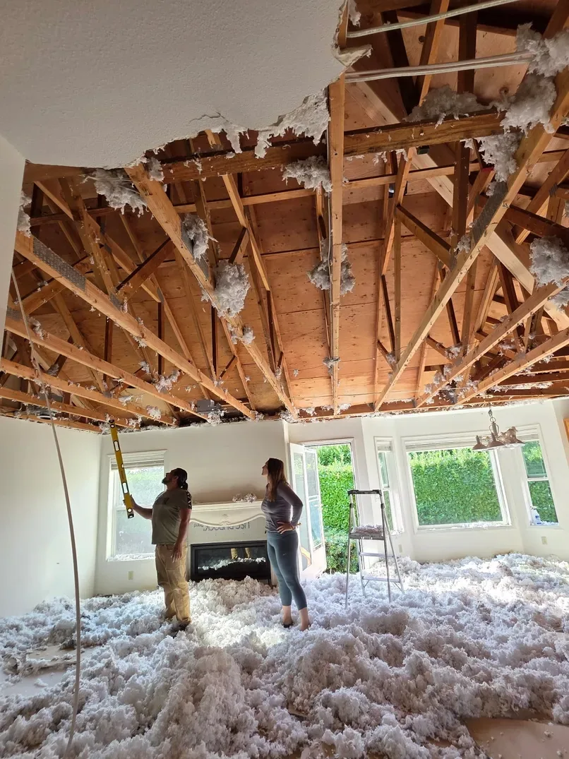 Pacific Builders team surveying a vaulted living room with the entire ceiling drywall removed, exposing original rafters and revealing structural opportunities for a major remodel.